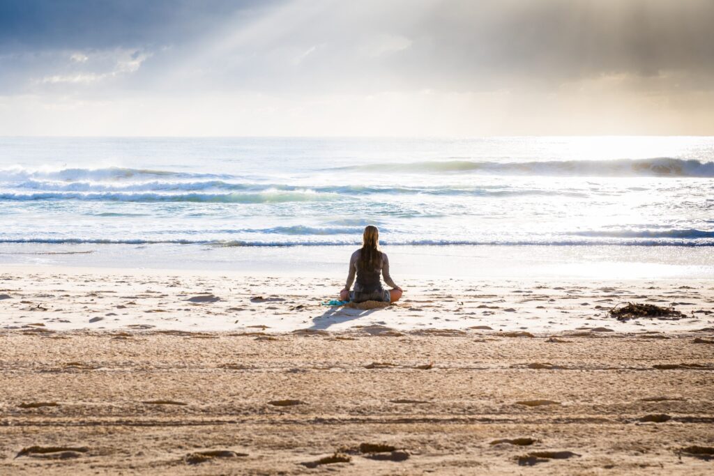 Woman meditating on a beach in blog about stop ruminating thoughts by erin moore centered one