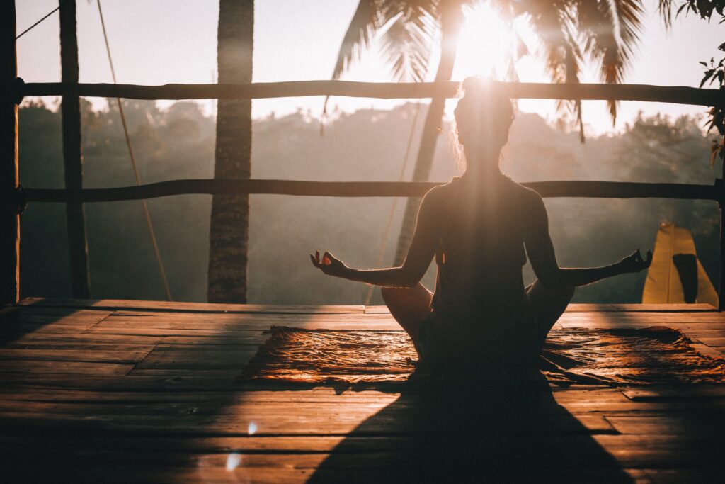 seated woman meditating at sunrise in blog about how to get rid of negative energy by erin moore centered one